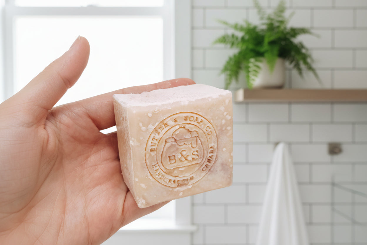 Hand holding a bar of soap with 'B & S' branding on a clean and bright bathroom background